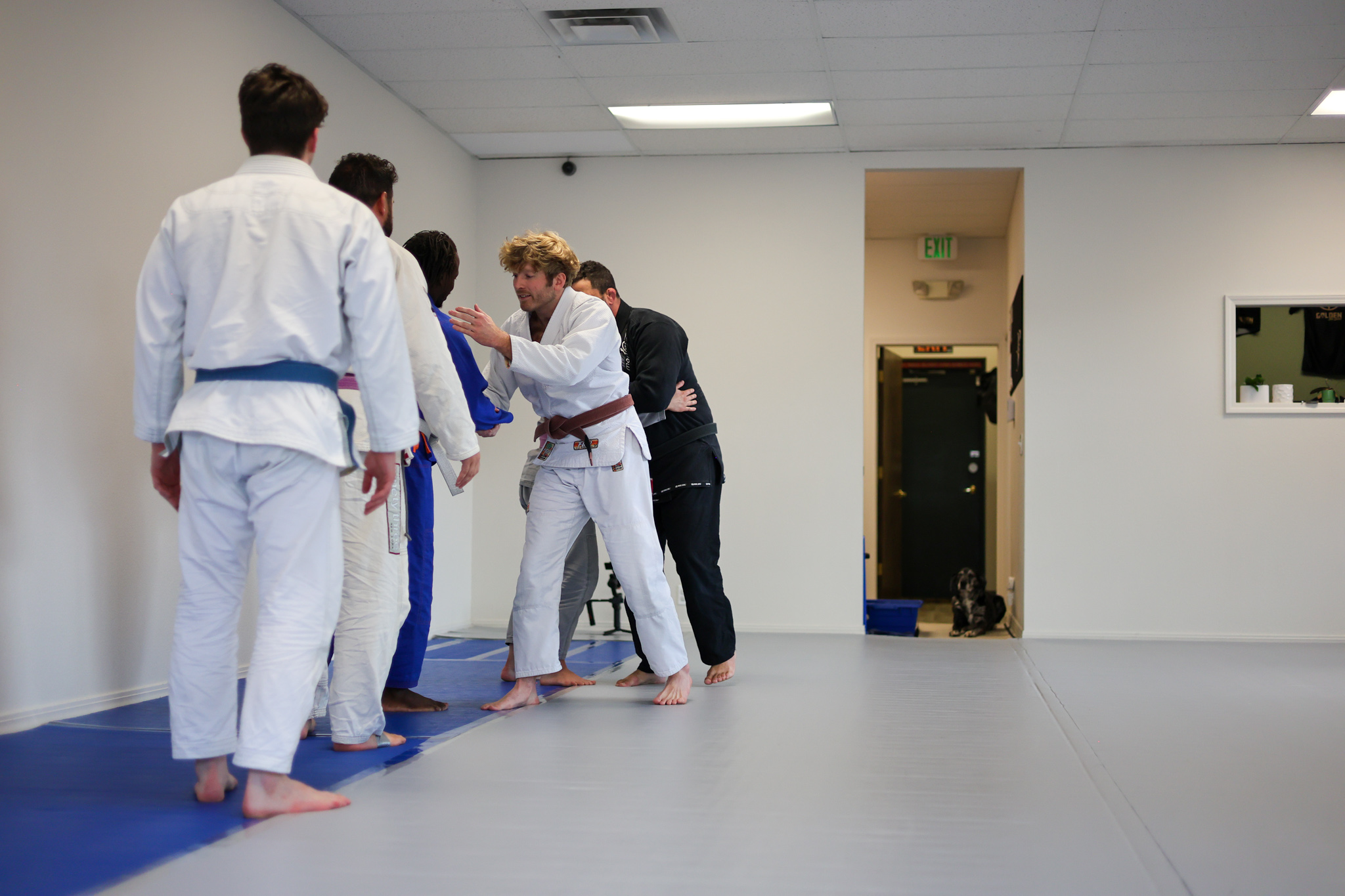 Members lining up at the end of class at Golden Jiu Jitsu, with the gym dog watching from the hallway